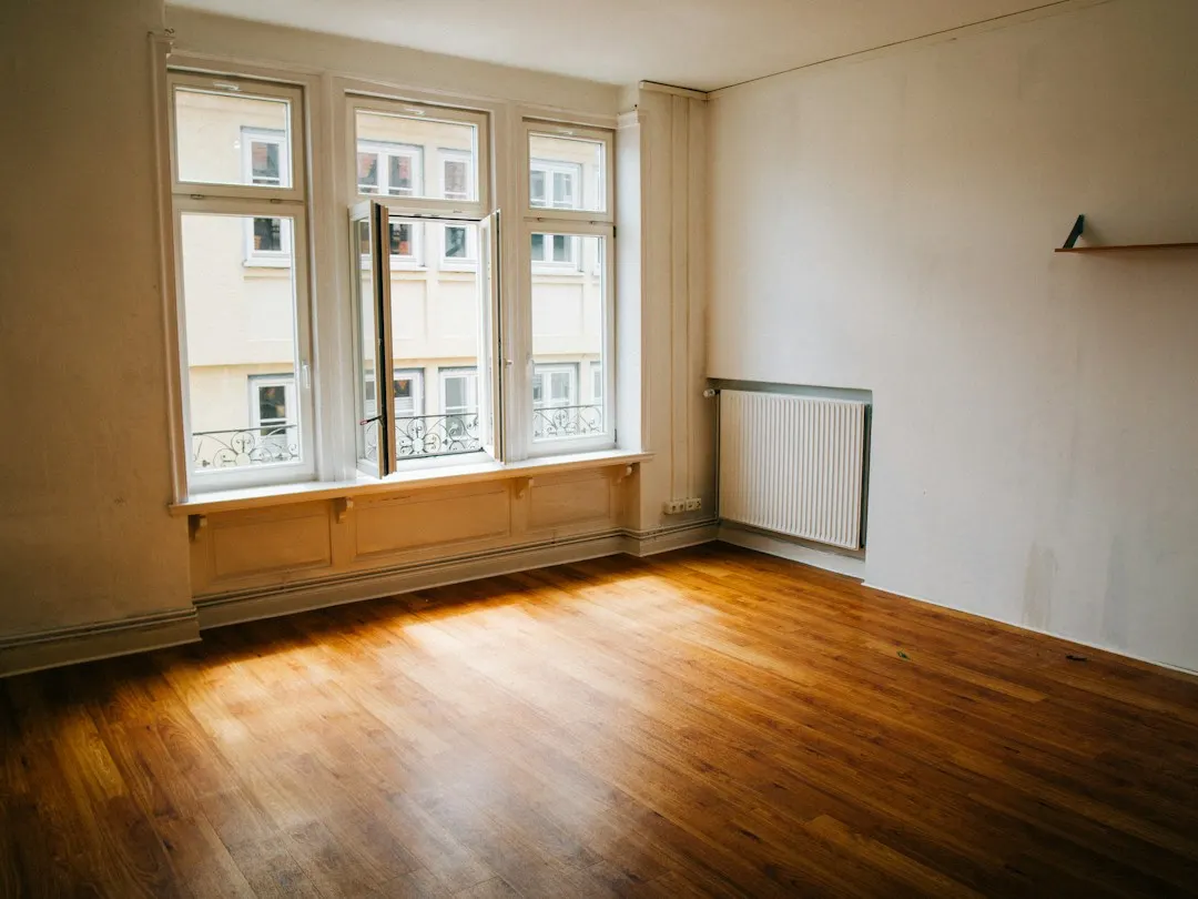 Leerer Altbauraum mit Holzdielen und hohen Sprossenfenstern im Nachmittagslicht