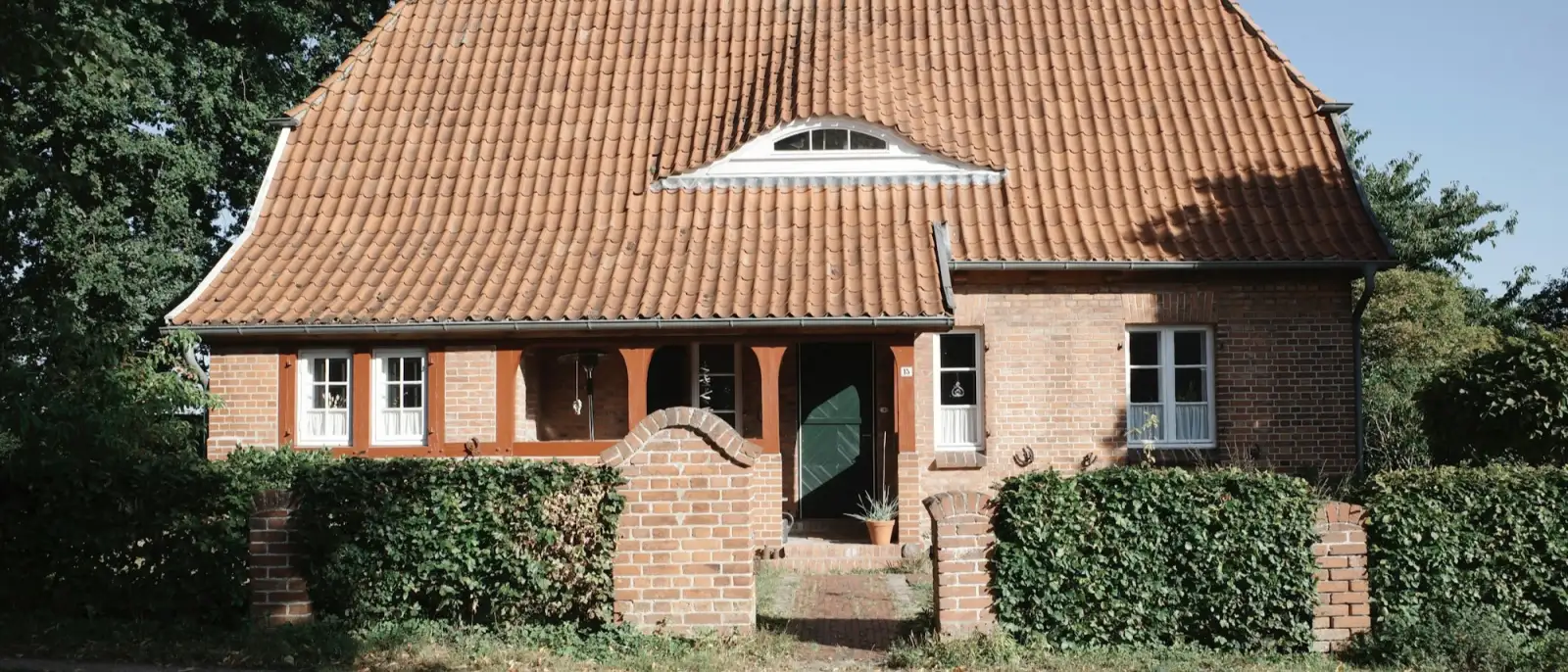 Backsteinhaus mit rotem Ziegeldach und grüner Haustür hinter einer Hecke in Schleswig-Holstein