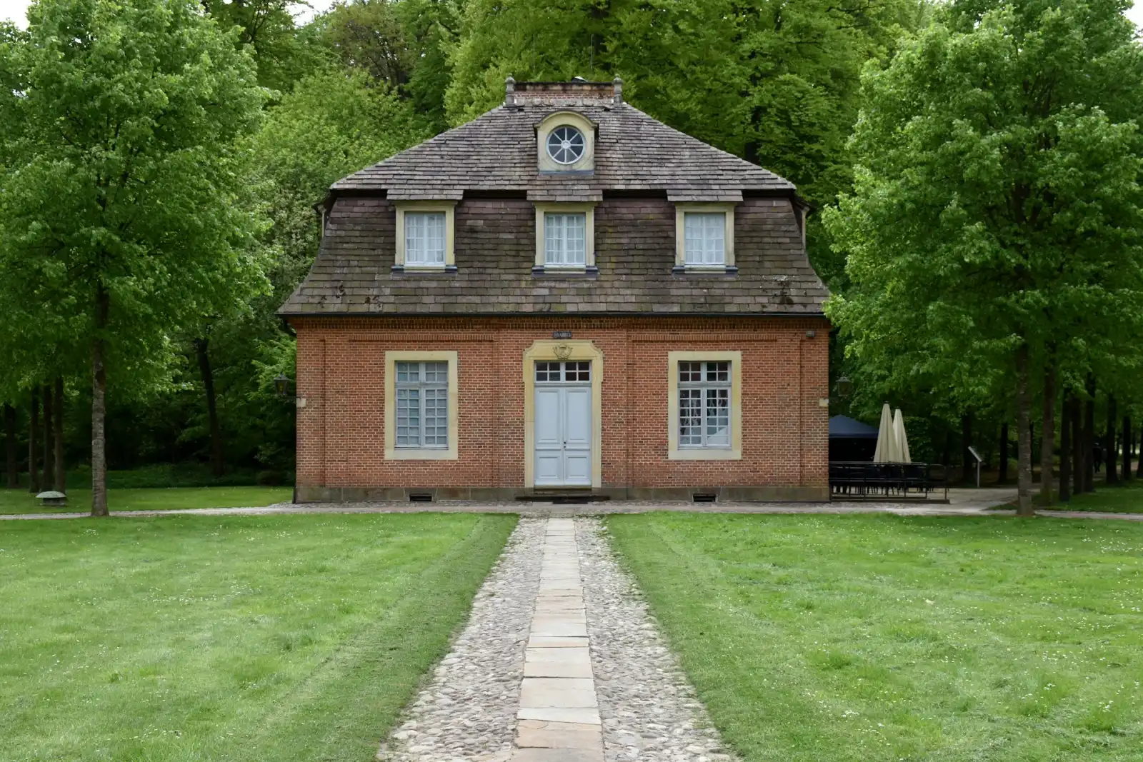 Backsteinhaus mit Walmdach, davor ein Plattenweg über den Rasen