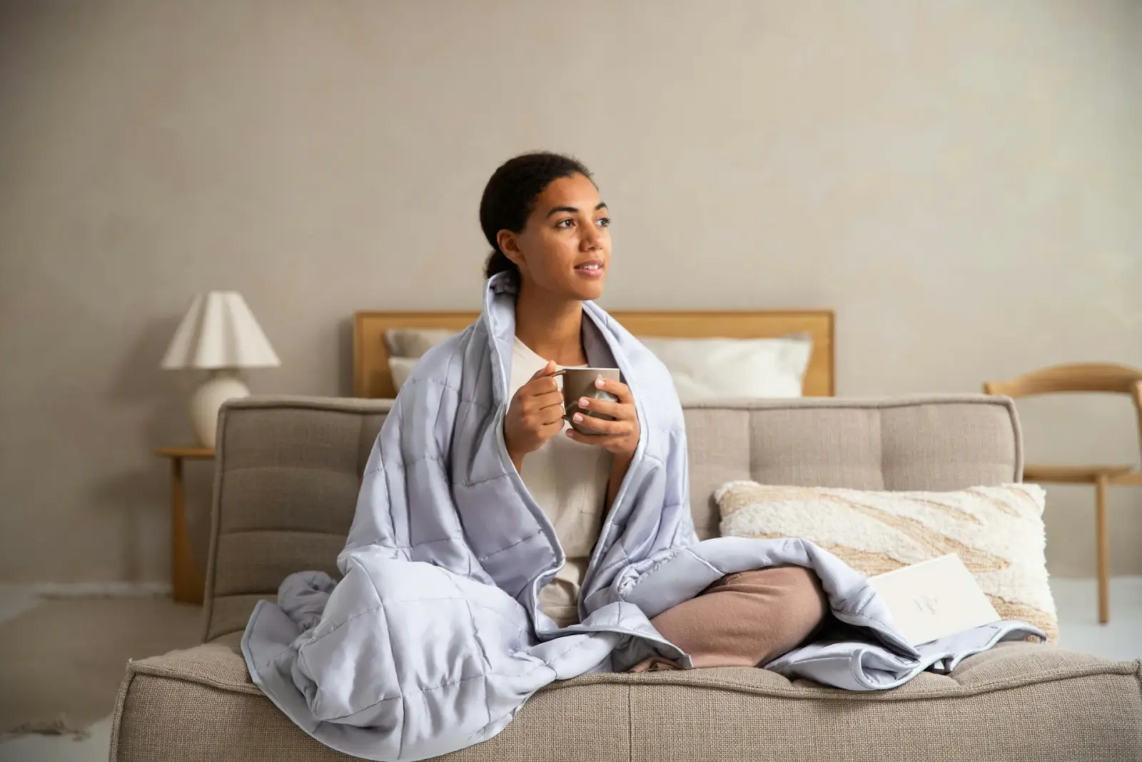 Frau sitzt in eine Decke gehüllt mit einer Tasse auf dem Sofa