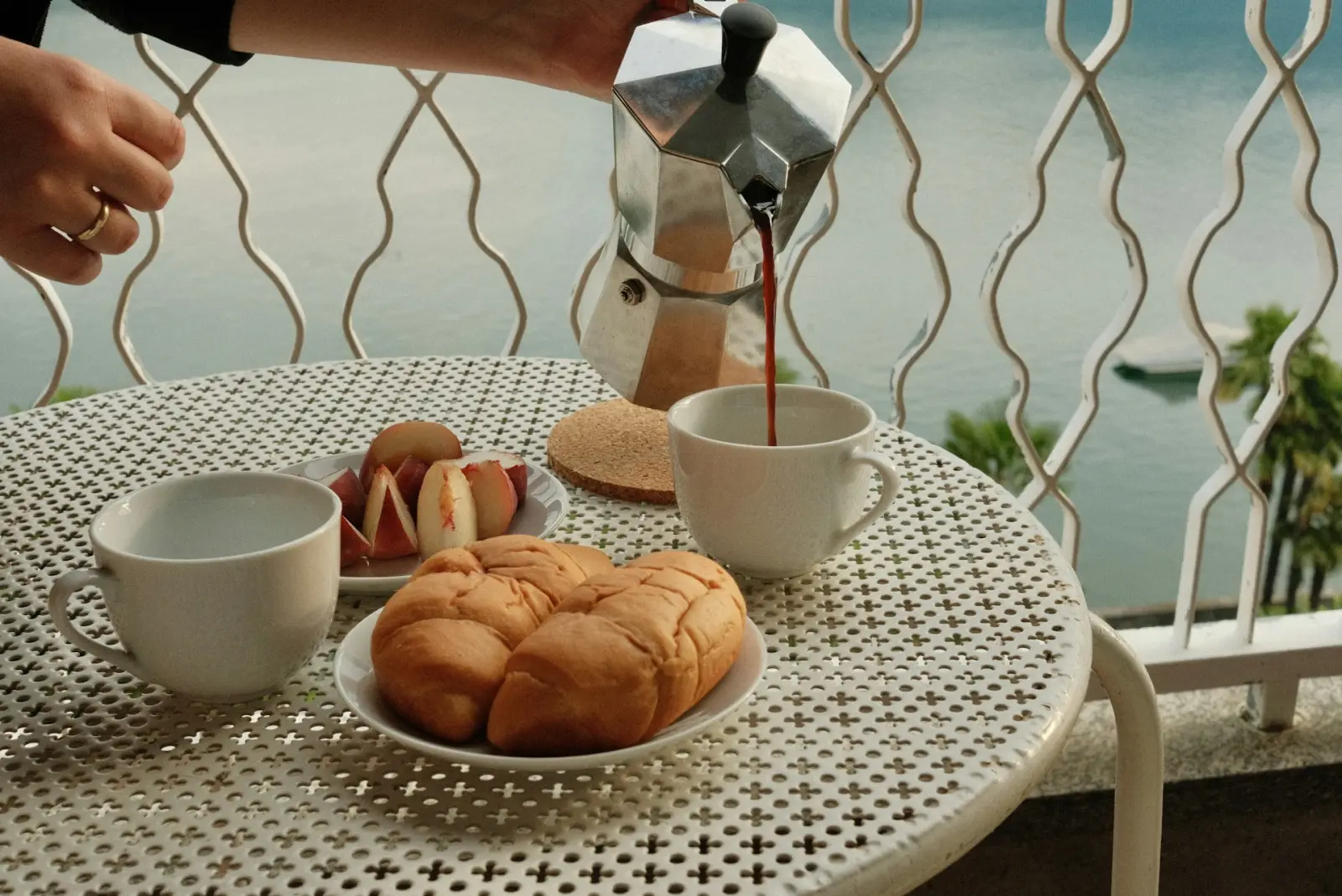 Kaffee wird eingeschenkt, daneben Gebäck auf einem Balkontisch